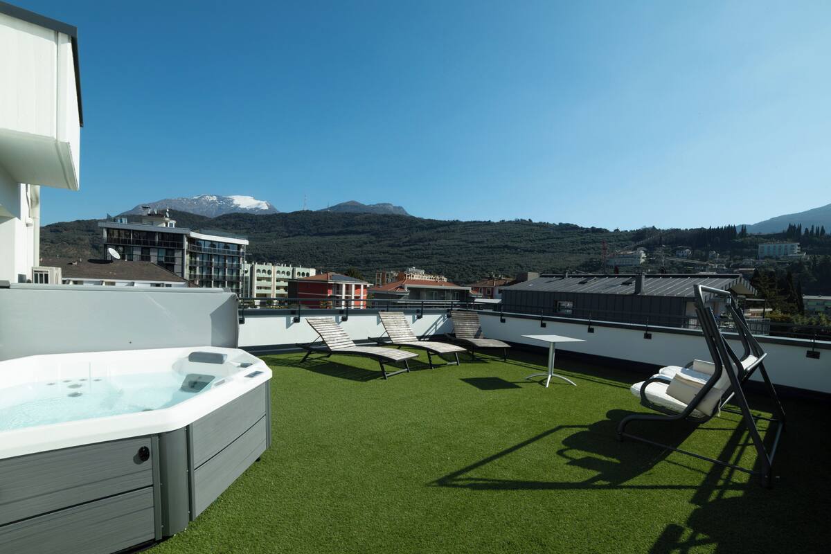 A rooftop terrace with a hot tub, lounge chairs, and a view of a mountain range.