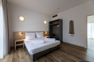 Una habitación de hotel moderna con una cama grande, mesitas de noche, un televisor integrado y un armario.