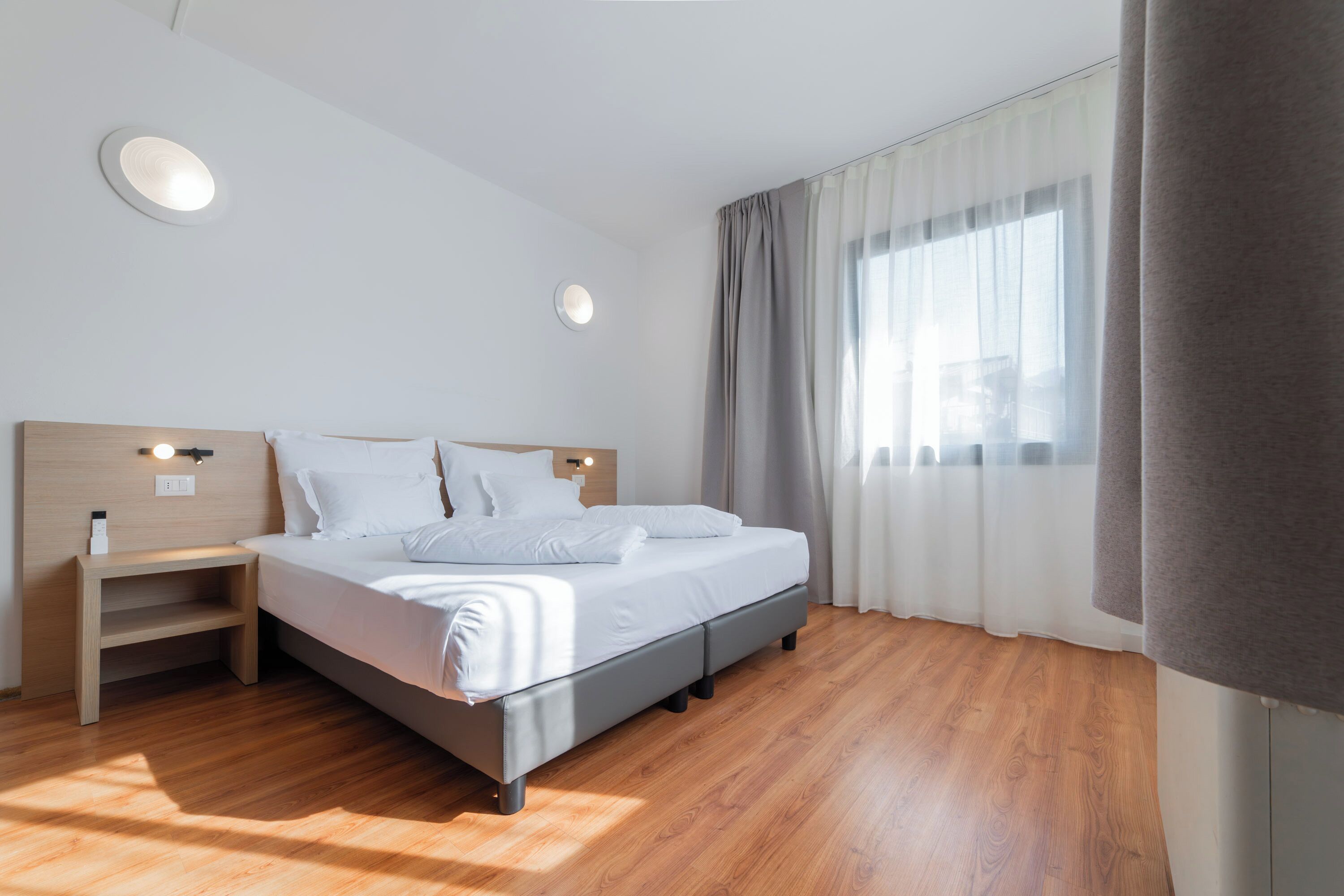 Ein modernes Schlafzimmer mit einem Bett, Nachttischen und einem Fenster mit Vorhängen.