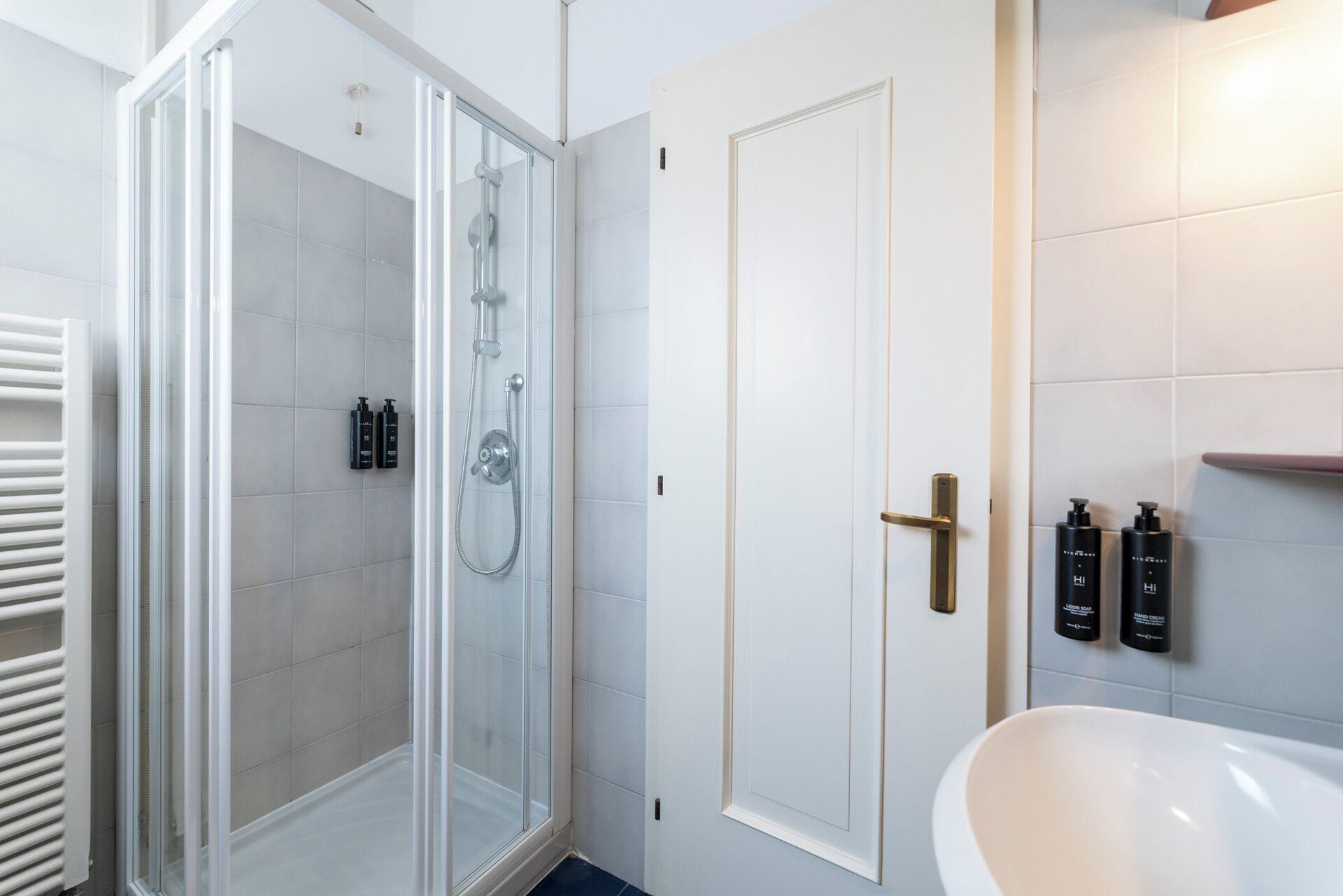 A modern bathroom with a glass-enclosed shower, a white sink, and toiletries on the wall.