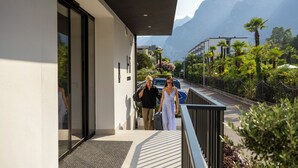 Ein modernes Gebäude mit Glastür, einem Balkon mit Metallgeländer und Blick auf Berge im Hintergrund.