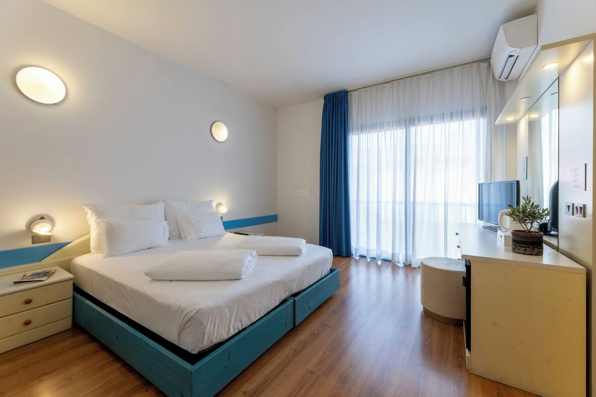 A modern hotel room with a large bed, bedside tables, a desk, and a mirror.