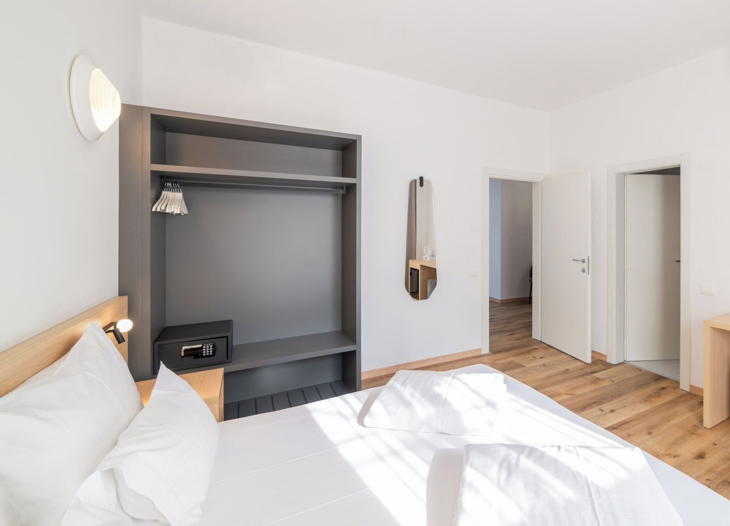 Un dormitorio moderno con cama, armario empotrado, mesita de noche con lámpara y espejo en la pared.
