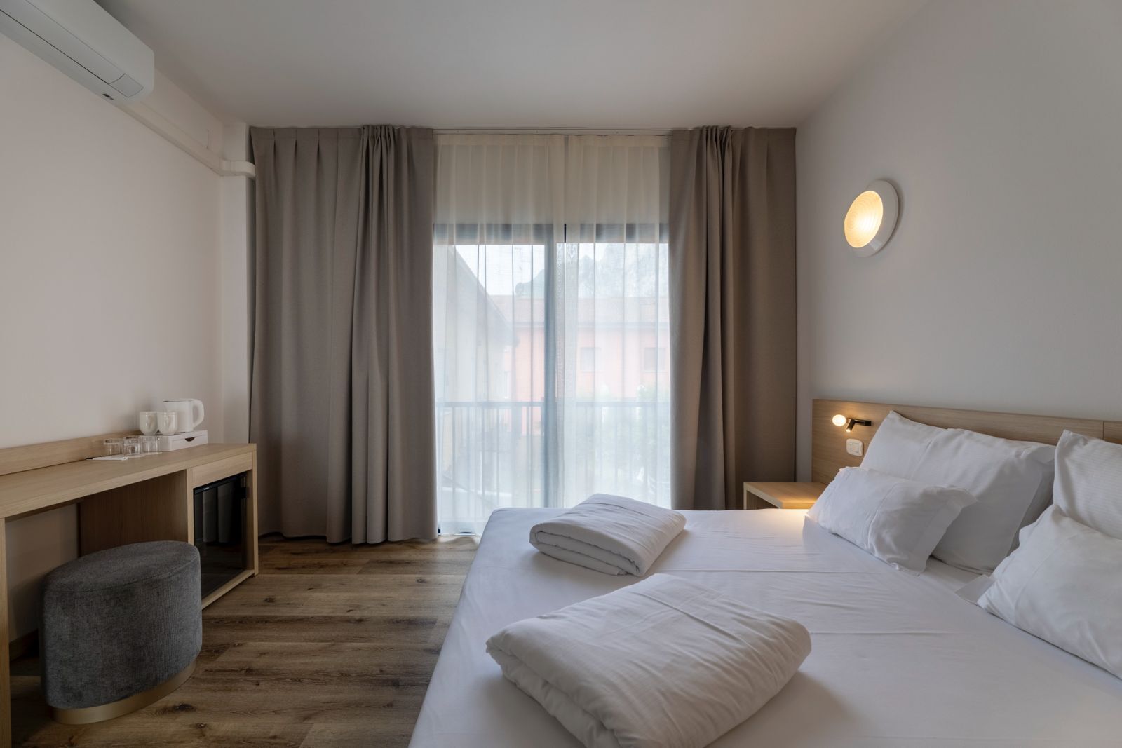 A hotel room with a bed, bedside table, and a window with curtains.