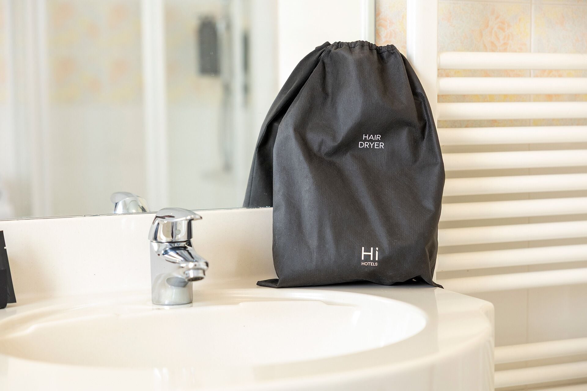 A bathroom sink with a hair dryer and a bag labeled "Hi Hotels" on the counter.