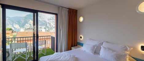 A hotel room with a large bed, a balcony with a view of mountains, and a small table with chairs.