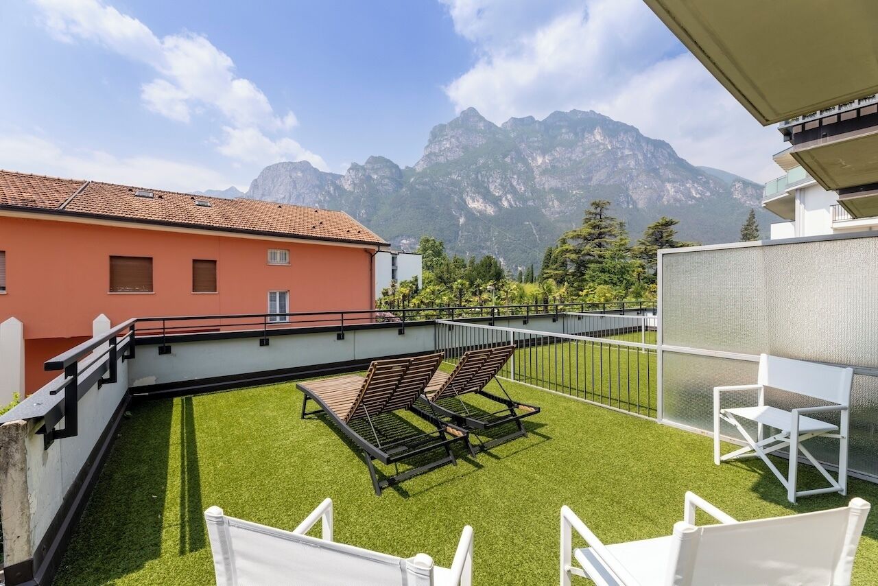 A rooftop terrace with artificial grass, two lounge chairs, and a view of mountains.