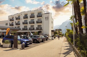 Un hotel de fachada blanca, con varios balcones y un estacionamiento con automóviles.