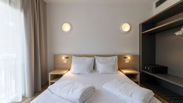 Una habitación de hotel con una cama grande, dos mesitas de noche, un armario y dos luces fijadas en la pared.