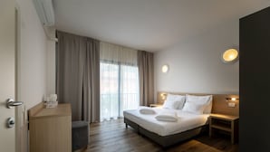 Ein Hotelzimmer mit Bett, Nachttischen, Schreibtisch und einem Fenster mit Vorhängen.
