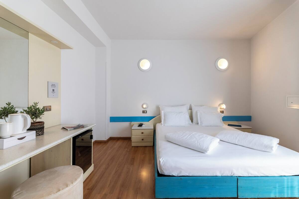 A hotel room with a bed, bedside tables, a desk, and a mirror.