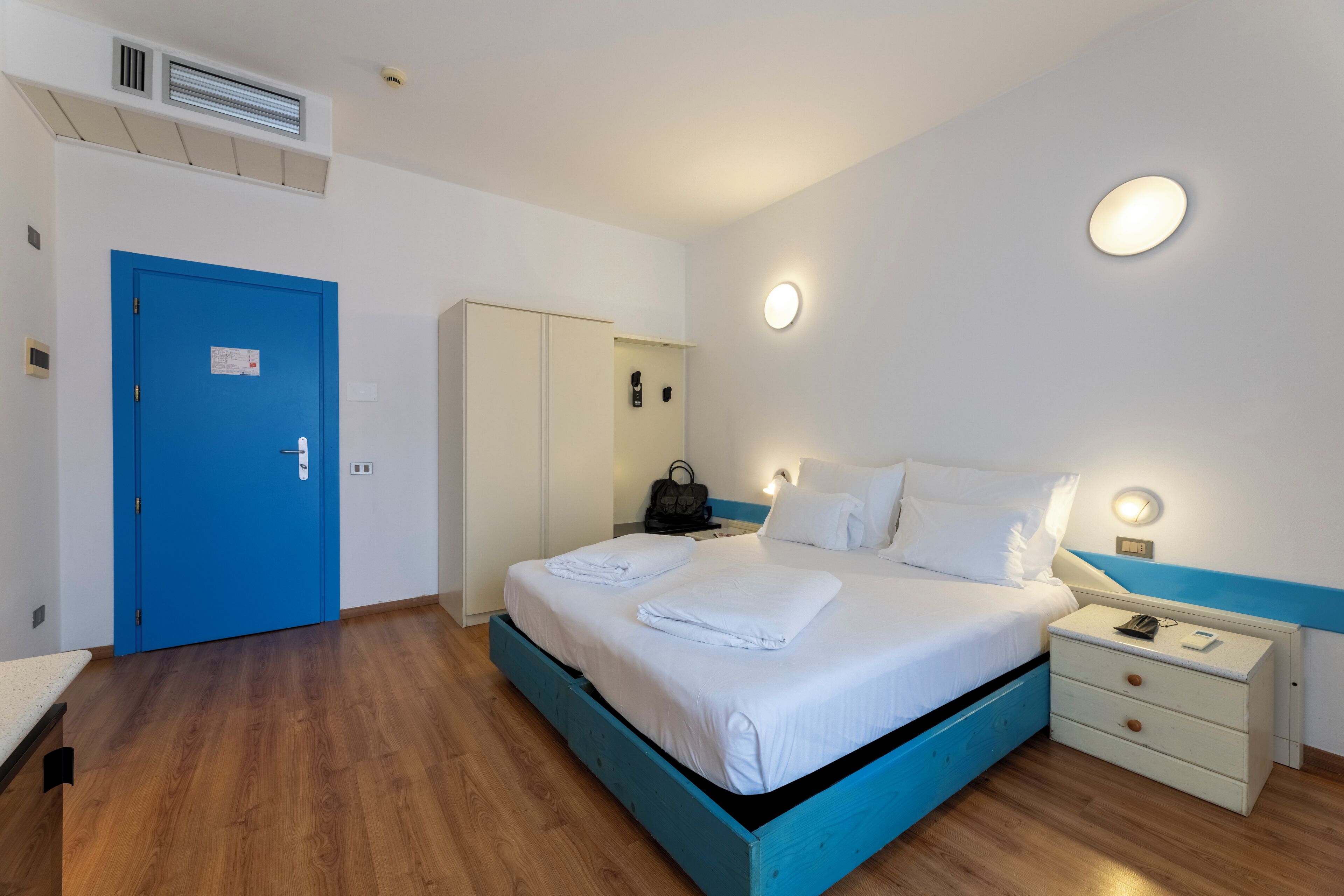 A bedroom with a blue bed frame, white bedding, a bedside table with a lamp, and a wardrobe.