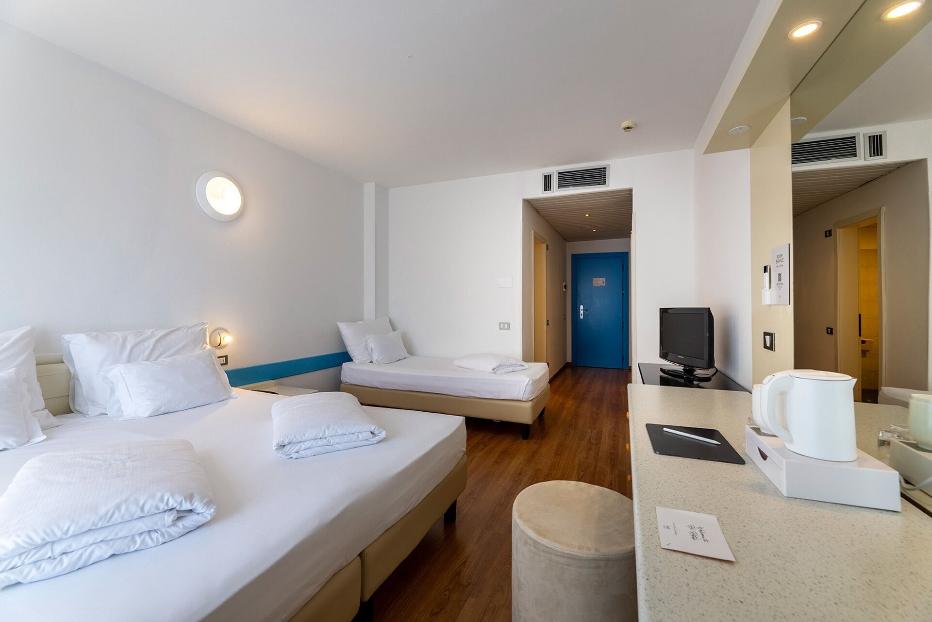 A hotel room with two beds, a desk with a computer, a TV, and a minibar.