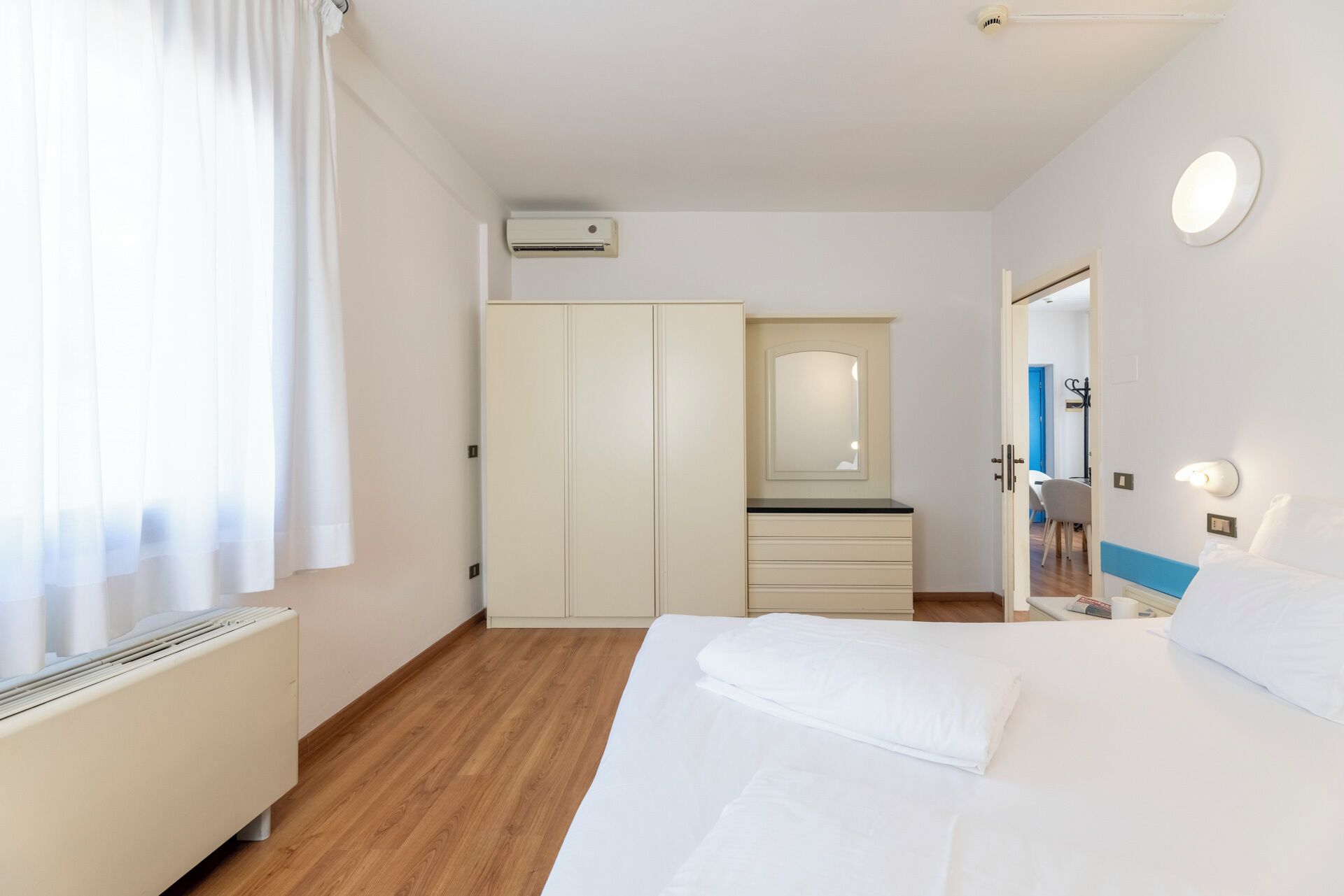 A hotel room with a bed, a bedside table, a mirror, a wardrobe, and an air conditioning unit.