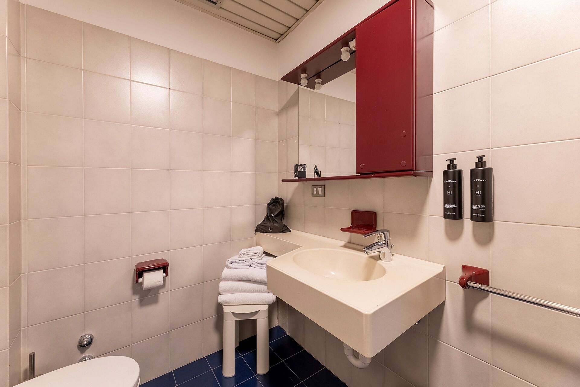 Un baño con un lavamanos blanco, un mueble rojo y dos botellas de crema para manos.