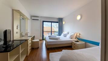 Une chambre d’hôtel comprenant un lit, des tables de chevet, un bureau avec un ordinateur, un miroir et une fenêtre donnant sur des immeubles.