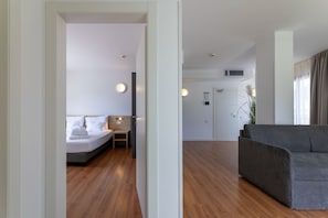 A modern hotel room with a bed, bedside table, and a grey sofa in the living area. - Hi Hotels Riva del Garda (Riva del Garda)