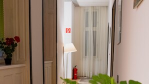 Un couloir avec un tapis à motifs, une plante en pot et un extincteur.