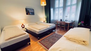 Une chambre d’hôtel avec deux lits, un bureau et une chaise. Il y a un tableau au mur et une fenêtre avec des rideaux.