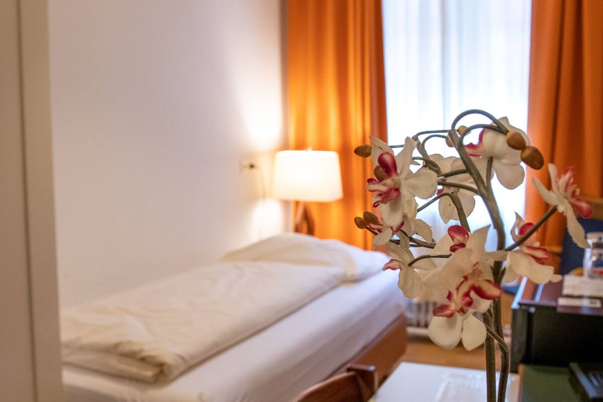Una habitación de hotel con una cama, un escritorio con lámpara y una orquídea en maceta.