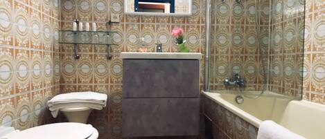 Une salle de bain avec des carreaux décorés, des toilettes, un lavabo avec un miroir et une baignoire.