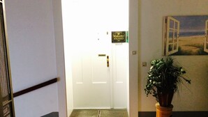 L’entrée d’un hôtel avec une porte blanche, un paillasson, un pot de fleurs et une fresque murale.