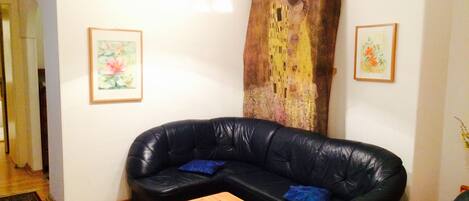 Un salon avec un canapé en cuir noir, une table basse en bois et deux œuvres d’art encadrées accrochées aux murs.