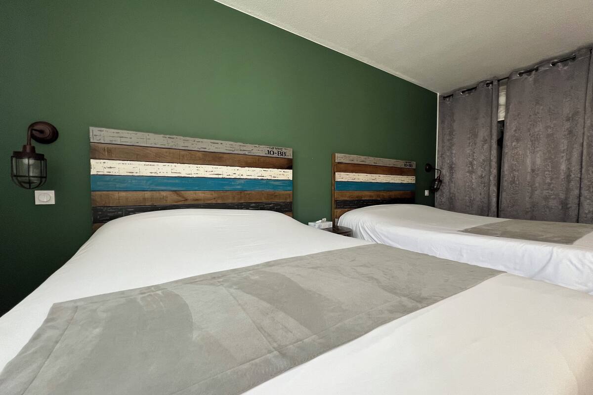 Une chambre avec deux lits, un mur vert et une tête de lit à motifs rayés.