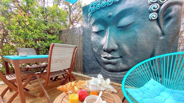 A wooden table with breakfast items, a blue chair, and a Buddha statue.