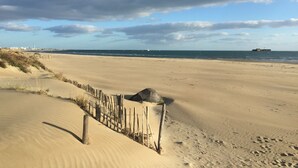 A sandy beach with a wooden fence and a lighthouse in the distance.