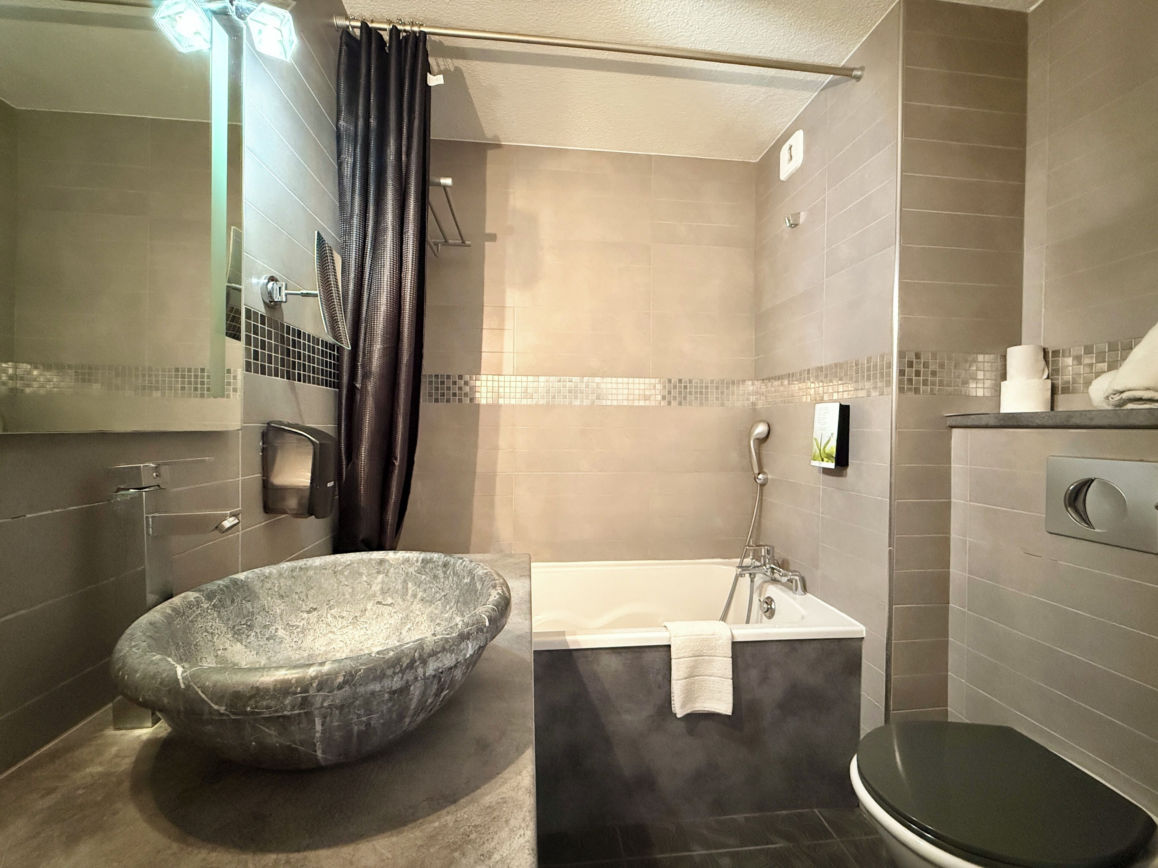 A bathroom with a large, round, stone basin, a modern bathtub, and a toilet.