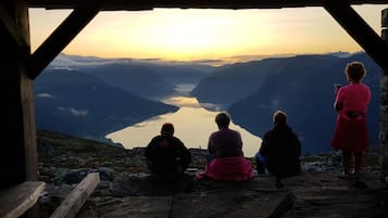A group of people sitting and standing on a rocky ledge overlooking a valley with a lake and mountains.