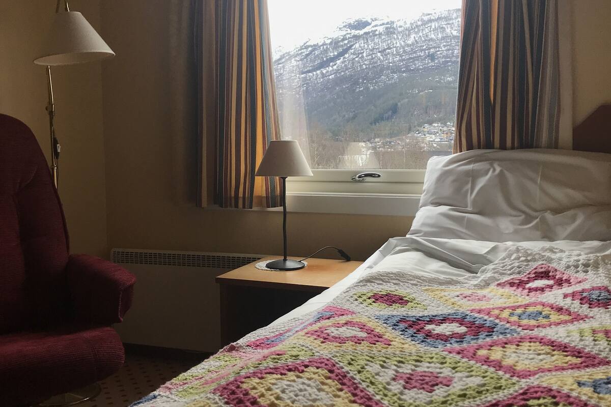 Habitación de hotel con cama, silla, lámpara y ventana con cortinas.