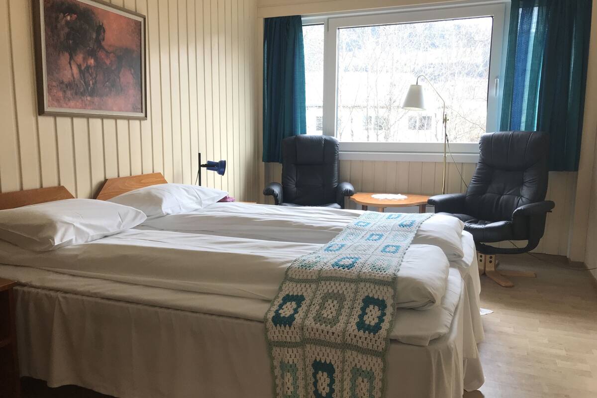 Una habitación de hotel con cama, dos sillas, una mesita, una lámpara y un cuadro en la pared.