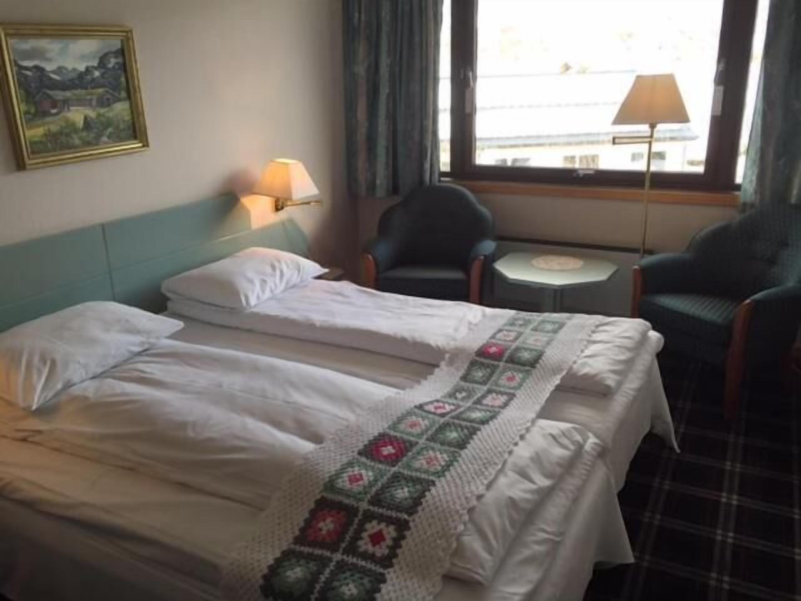 A hotel room with a bed, two chairs, a small table, and a window with curtains.