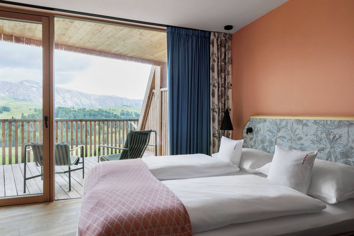 A bedroom with two beds, a balcony with chairs, and a view of mountains.