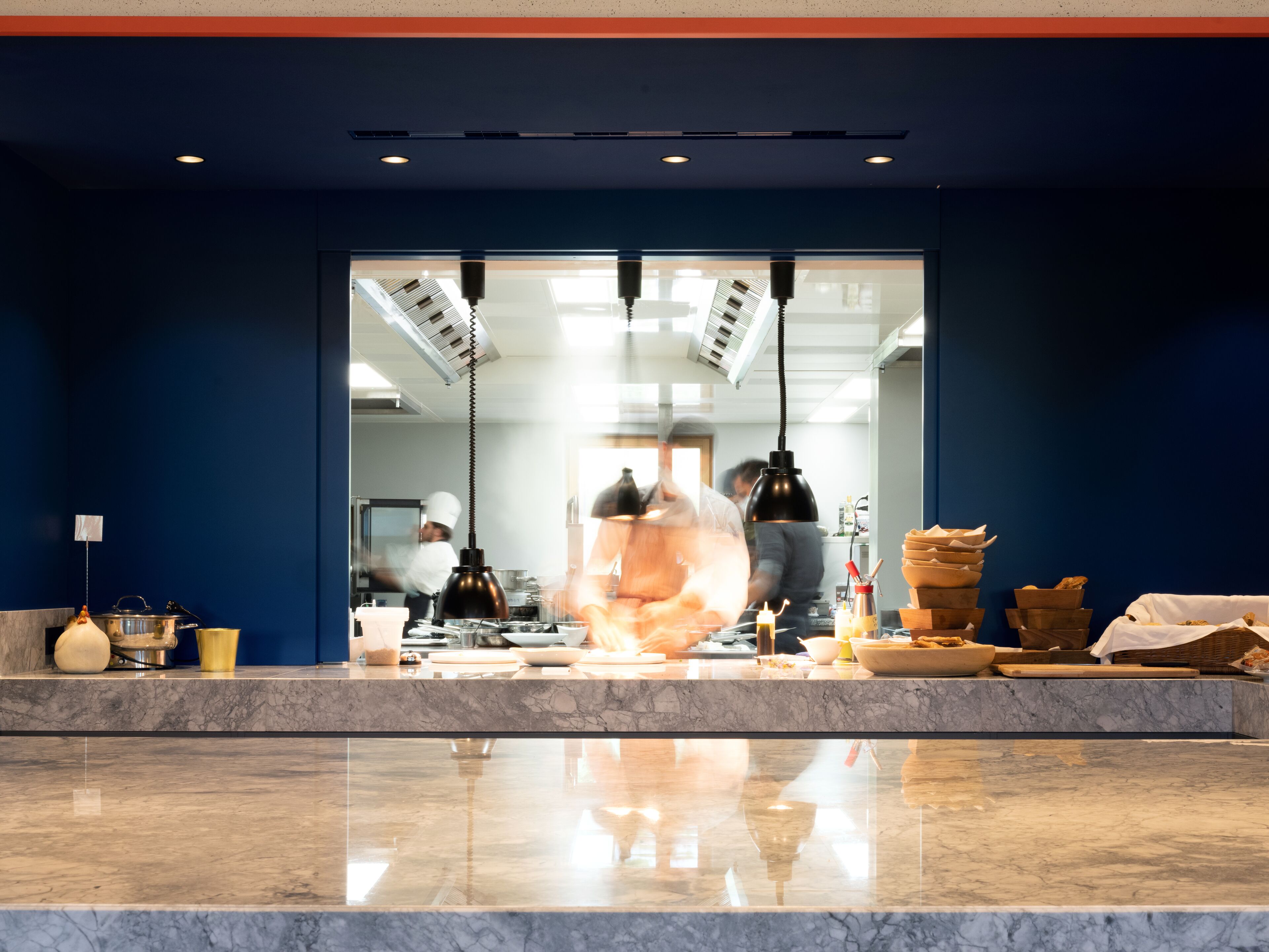A kitchen with marble countertops, a chef at work, and various cooking utensils and ingredients.