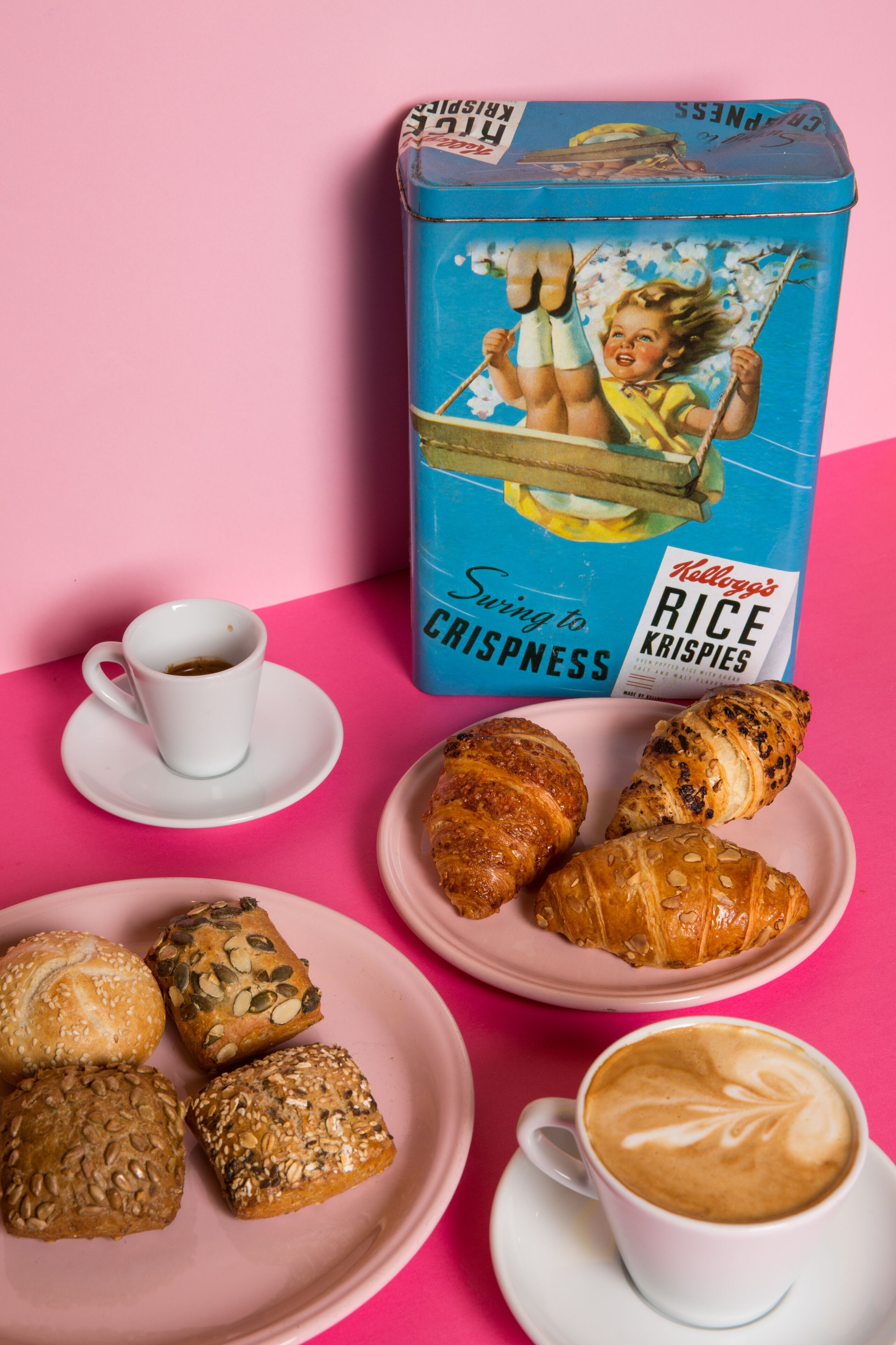 A box of Kellogg's Rice Krispies with a child swinging on a swing, a cup of coffee, and various pastries on a pink table.