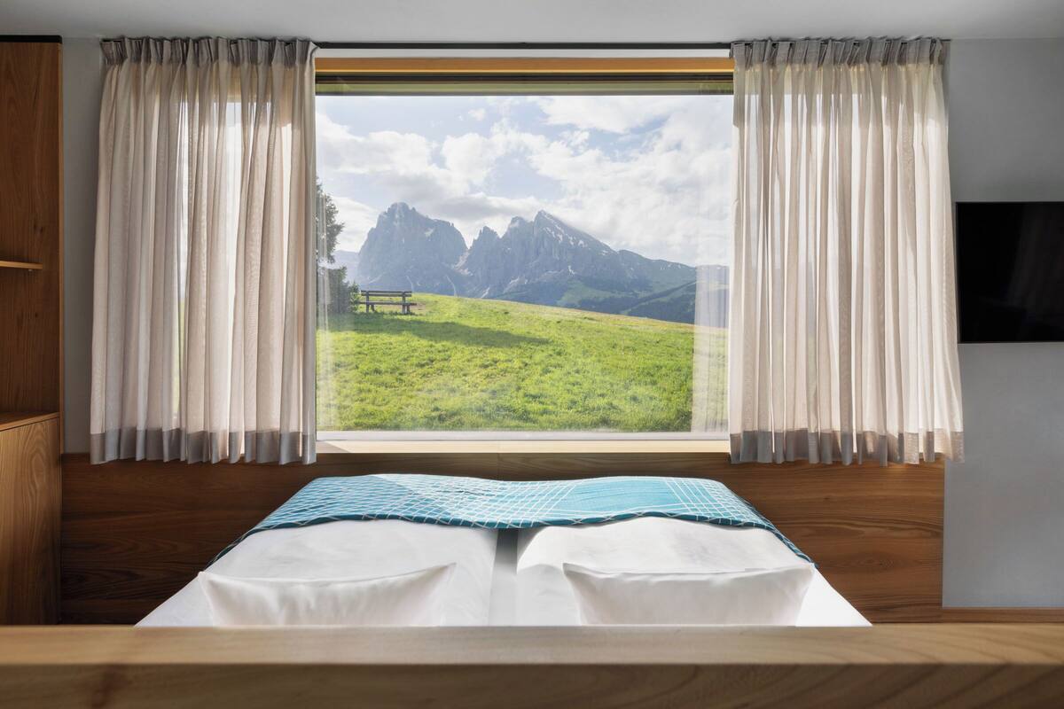 A bedroom with a large window, wooden bed frame, and curtains.