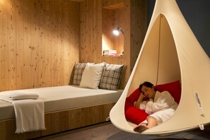 A room with a bed, a hanging chair, and a shelf with books. - Icaro Hotel (Castelrotto)