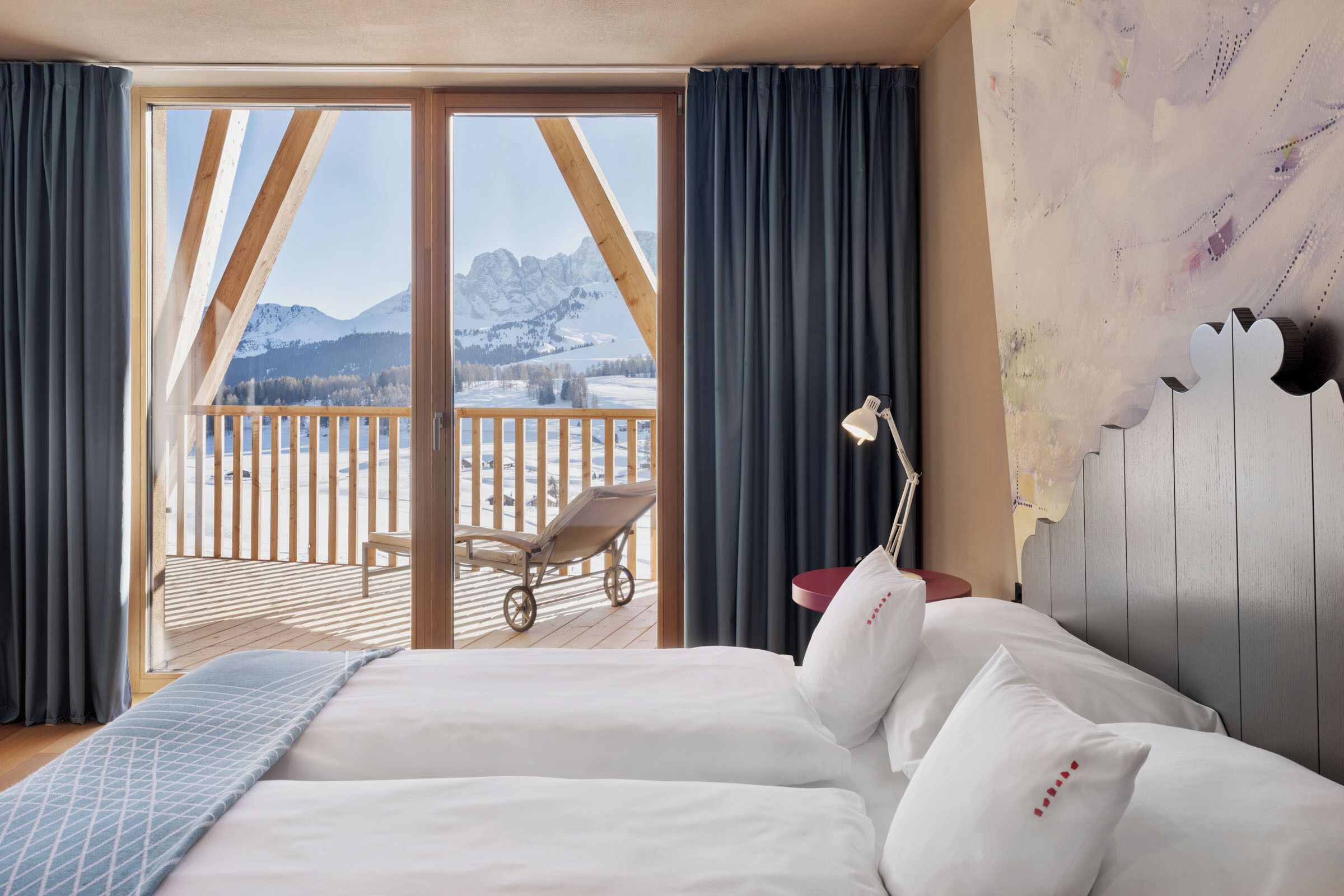 Een hotelkamer met een bed, een bureau, een stoel en uitzicht op een besneeuwd berglandschap.