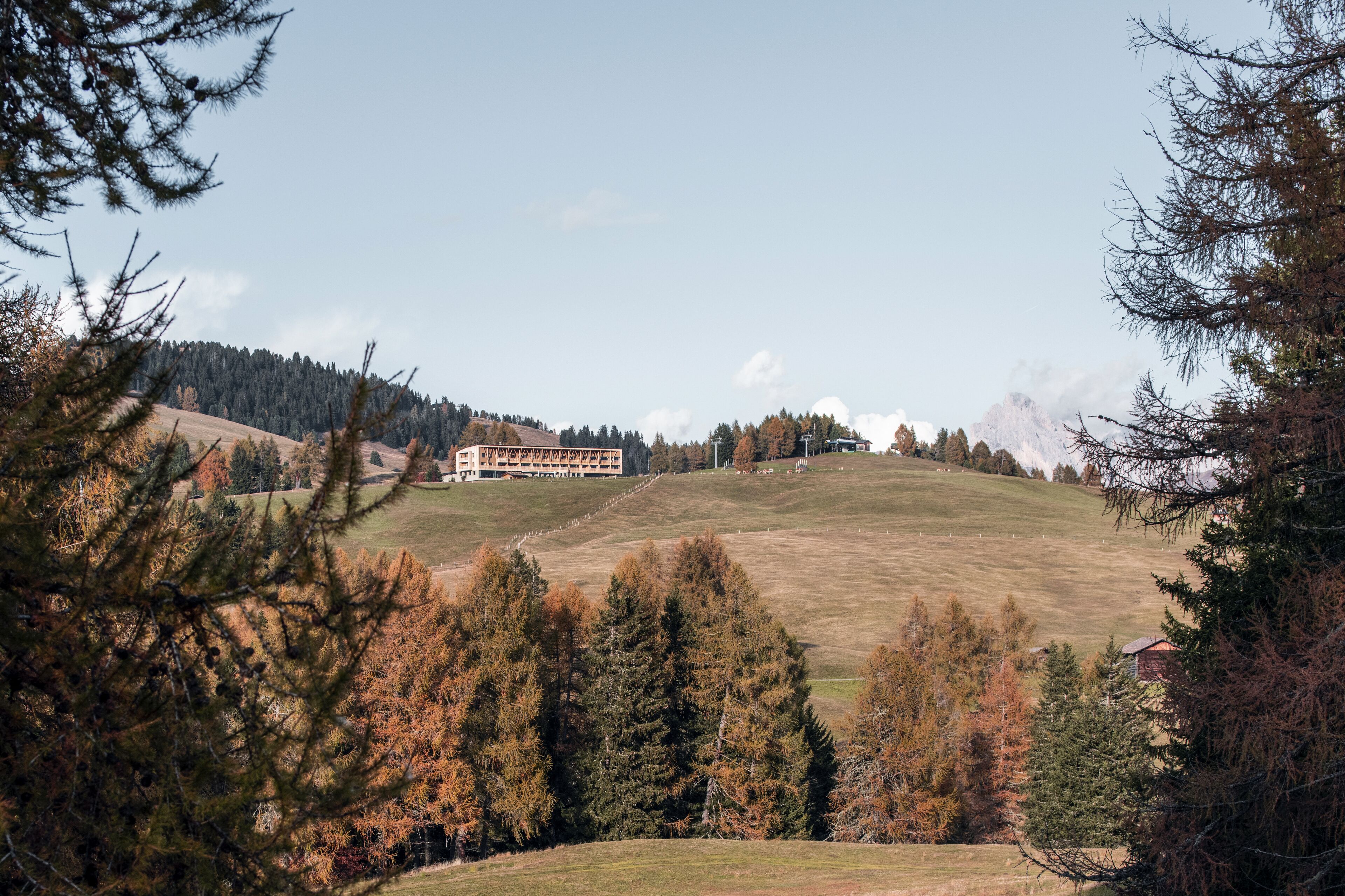 A building with a long, low profile, surrounded by a hilly landscape with trees and a clear sky.