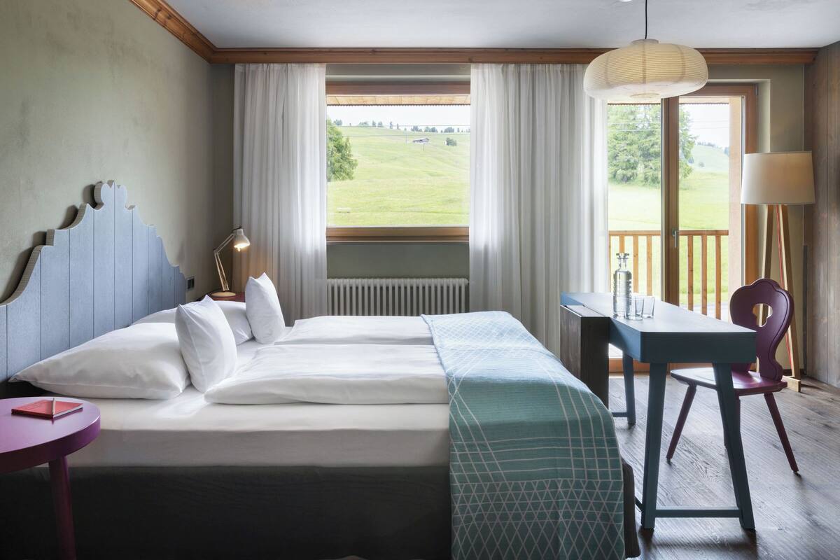 A hotel room with a large bed, a desk, and a view of a green landscape.