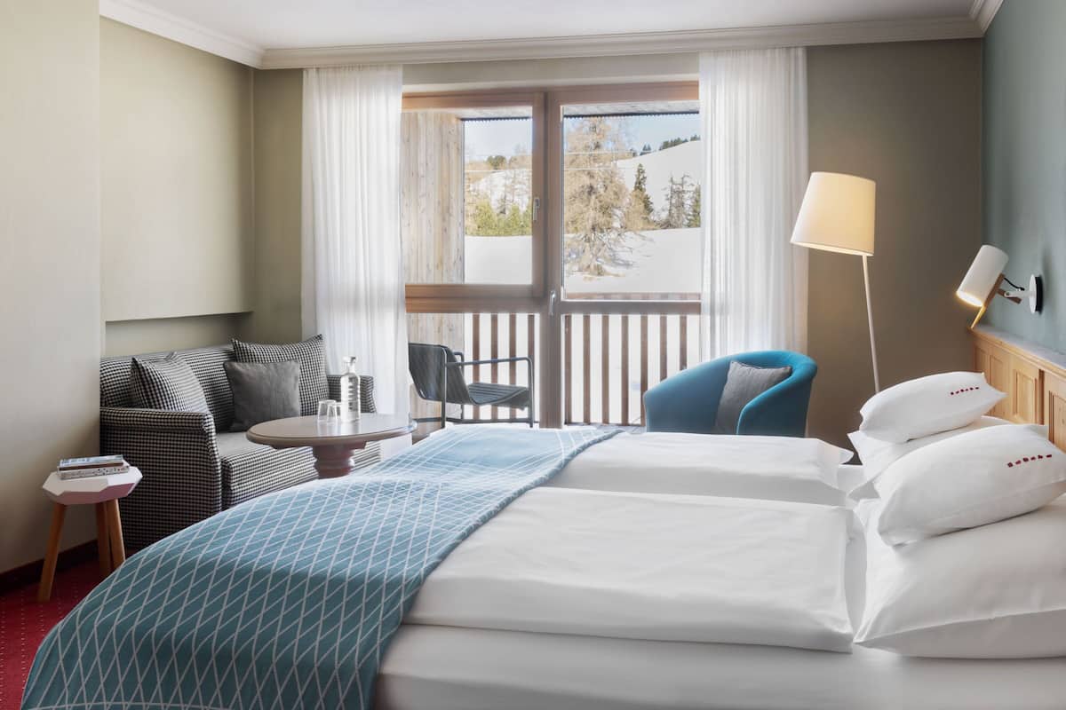 A hotel room with two beds, a sofa, a chair, a small table, and a lamp.