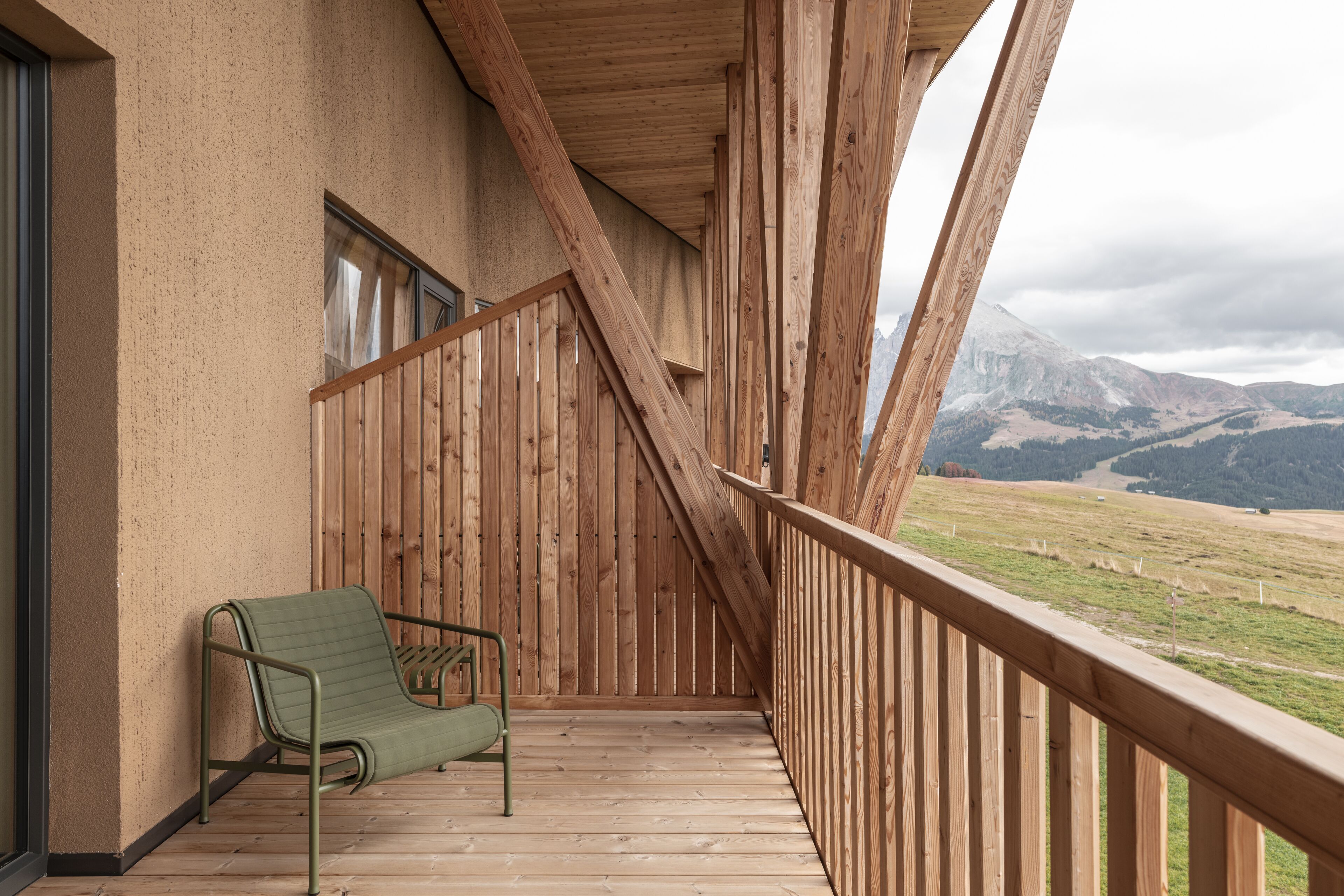 Ein Holzbalkon mit einem grünen Stuhl, Holzgeländern und Blick auf Berge.