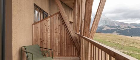 Ein Holzbalkon mit einem grünen Stuhl, Holzgeländern und Blick auf Berge.