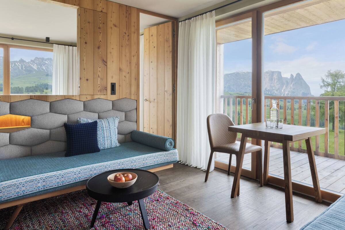 A modern room with a wooden wall, a sofa, a dining table, and a view of mountains.