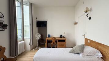 Un dormitorio con cama, escritorio de madera, silla y televisión en la pared.