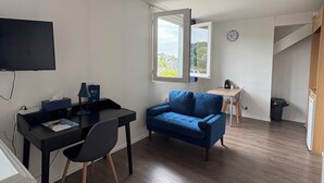 A room with a desk, a blue sofa, a TV, and a window with a view. - Hôtel de Bretagne (Redon)
