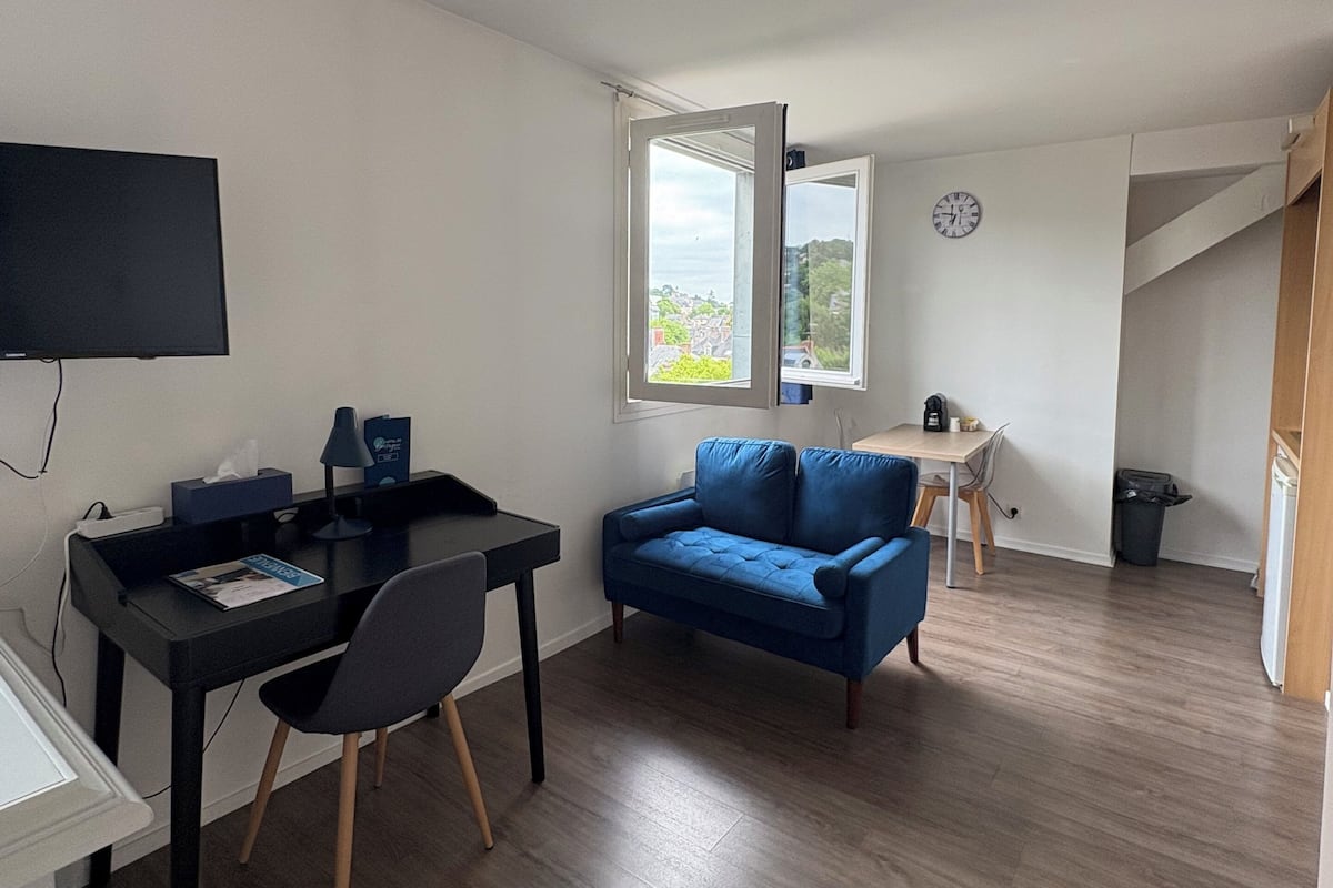 Ein Zimmer mit Schreibtisch, einem blauen Sofa, einem Fernseher und einem Fenster mit Blick.
